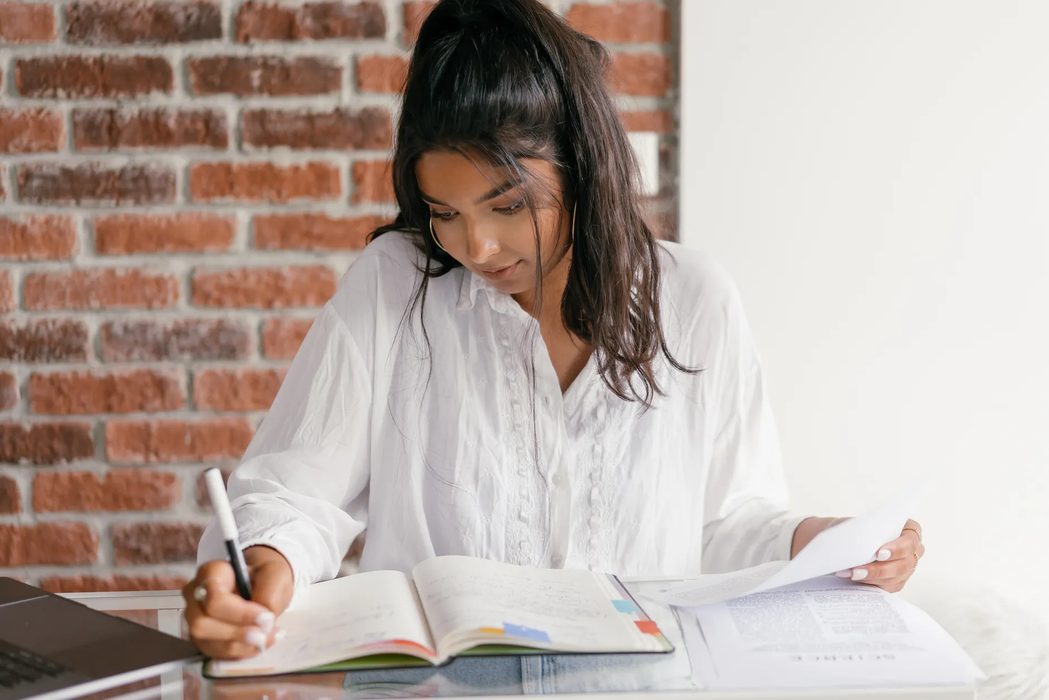 A student at a desk reviewing printed forms and notes beside a laptop