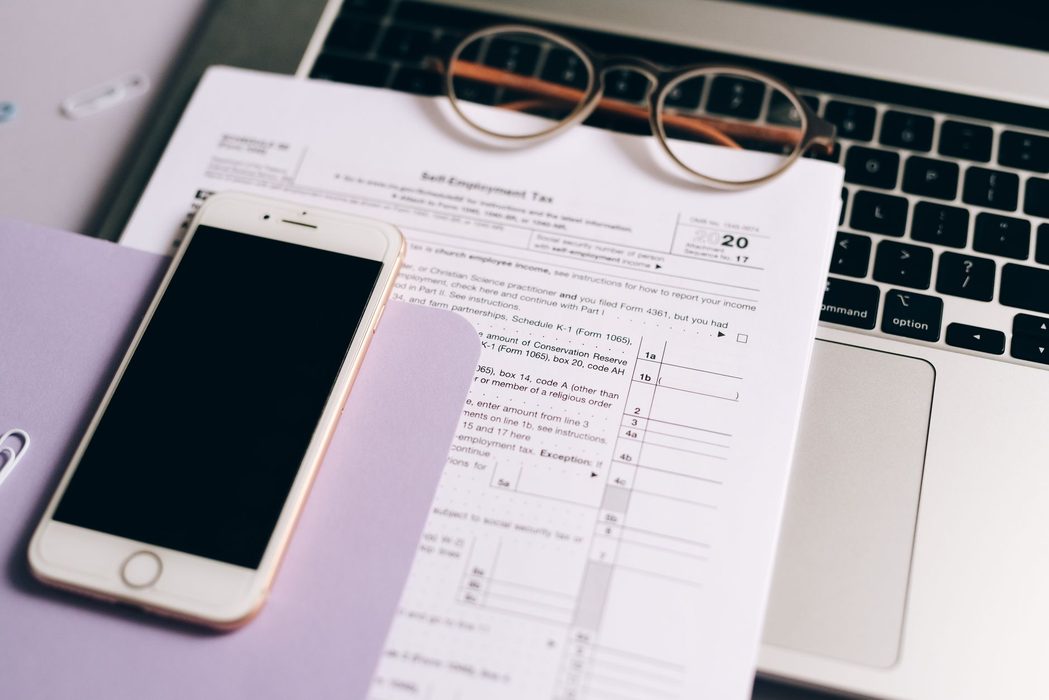 Printed tax forms, a notebook and a laptop arranged on a desk